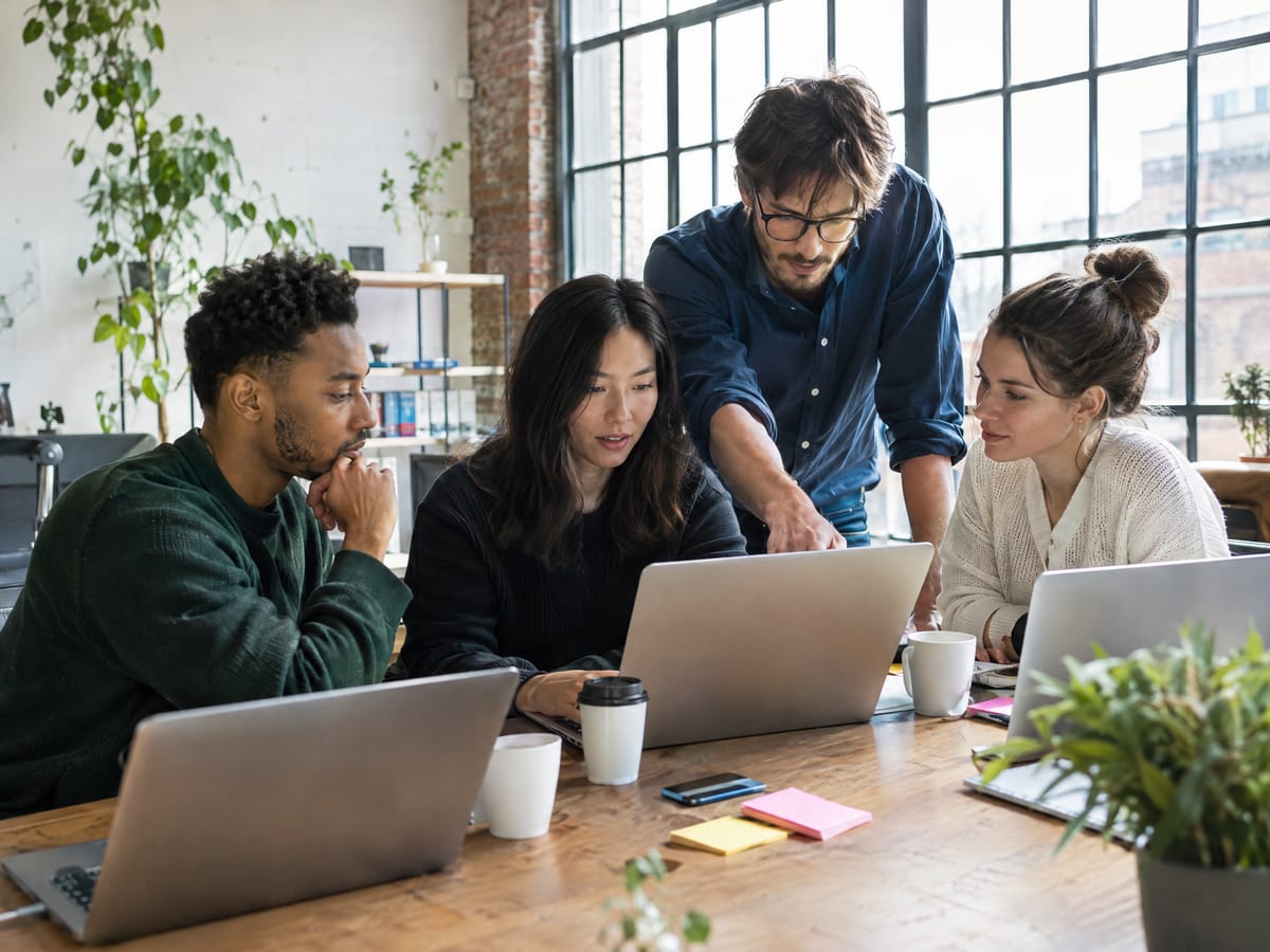 Four colleagues working around laptops at a shared table in a loft office
